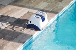 robot-electrique-piscine-equipement-nettoyage-aspirateur-lbap robot électrique de piscine blanc et bleu au bord de l'eau sur terrasse en bois avec cable
